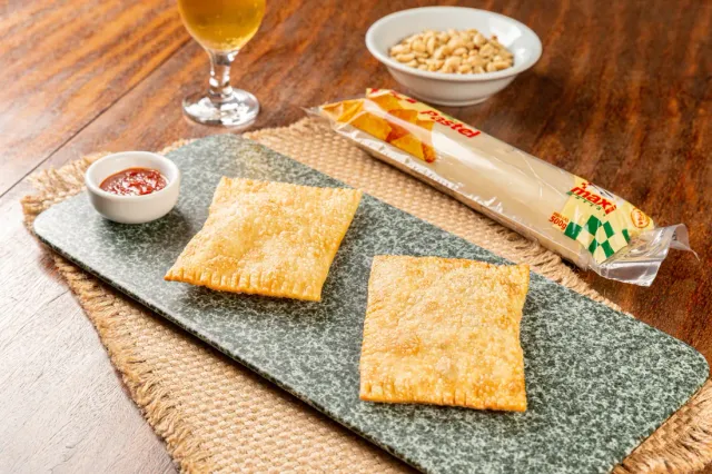 Pastéis fritos sobre tábua de pedra, com a embalagem da massa ao lado